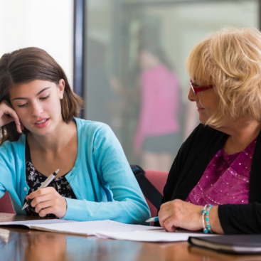 Schülerin und Lehrerin sitzen am Tisch zusammen