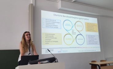 Antonia Landgraf an einem Rednerpult mit großer Beamer-Präsentation im Hintergrund