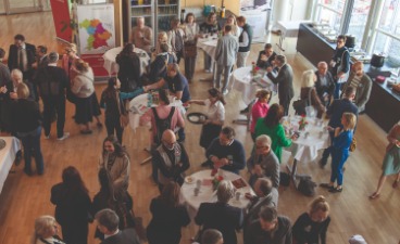 Blick von oben auf viele Menschen, die in kleinen Grüppchen zusammenstehen und netzwerken